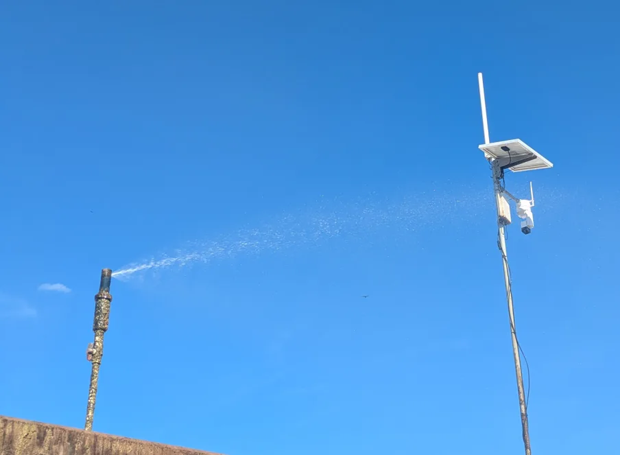 Solar-powered Altamus LiDAR sensor on a pole against a blue sky, with a dust-suppression water spray nearby