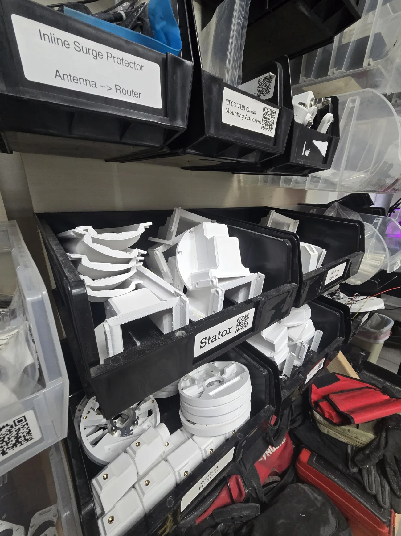 Labeled bins of white 3D-printed sensor parts, including stators and mounting brackets, ready for assembly