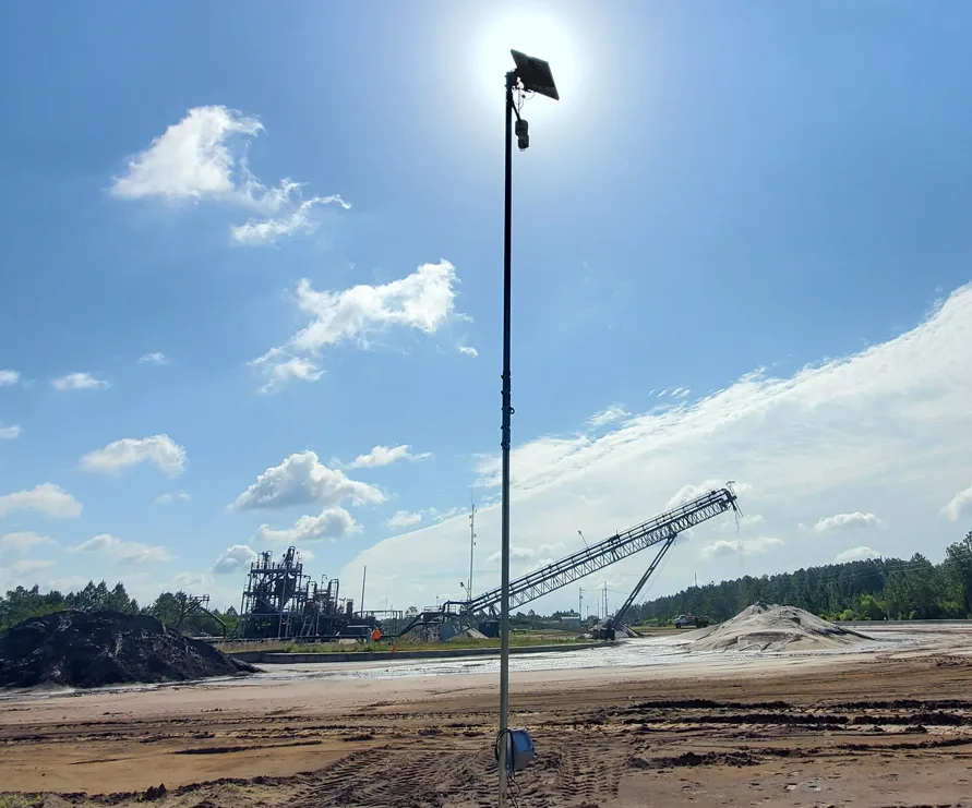 Altamus LiDAR sensor with a small solar panel mounted on a tall pole above an open sand and aggregate yard, with a stacker conveyor and stockpiles behind it