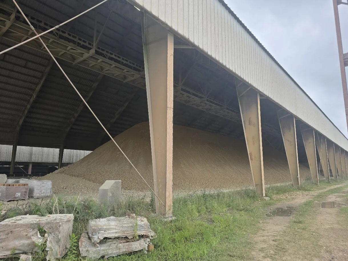 Large raw material stockpile under an open-sided storage building at a cement plant