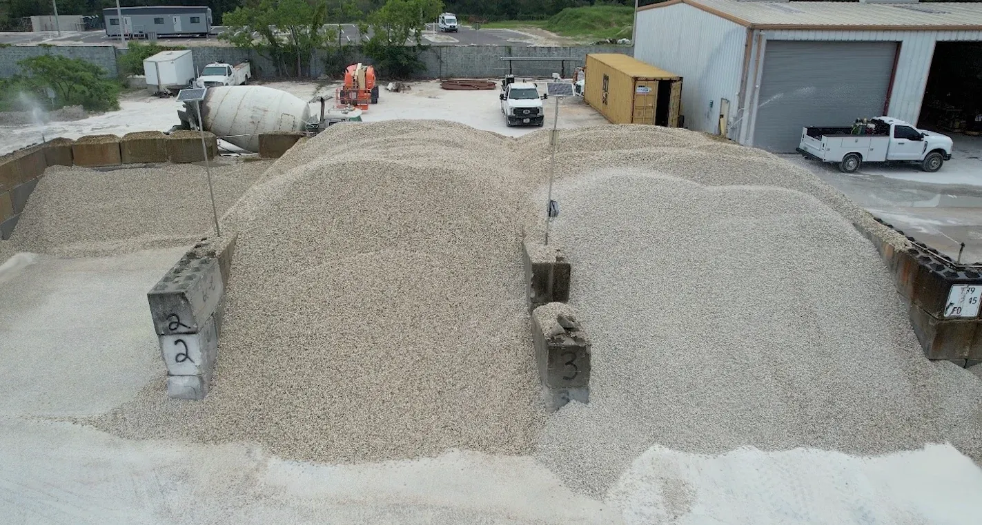 Aggregate stockpile bins at a ready-mix plant before LiDAR scanning, with pole-mounted EOS2 sensors