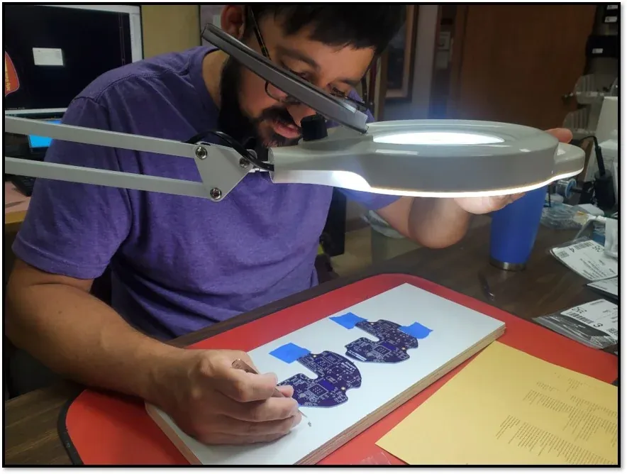 Altamus engineer inspecting a circuit board under a magnifier lamp