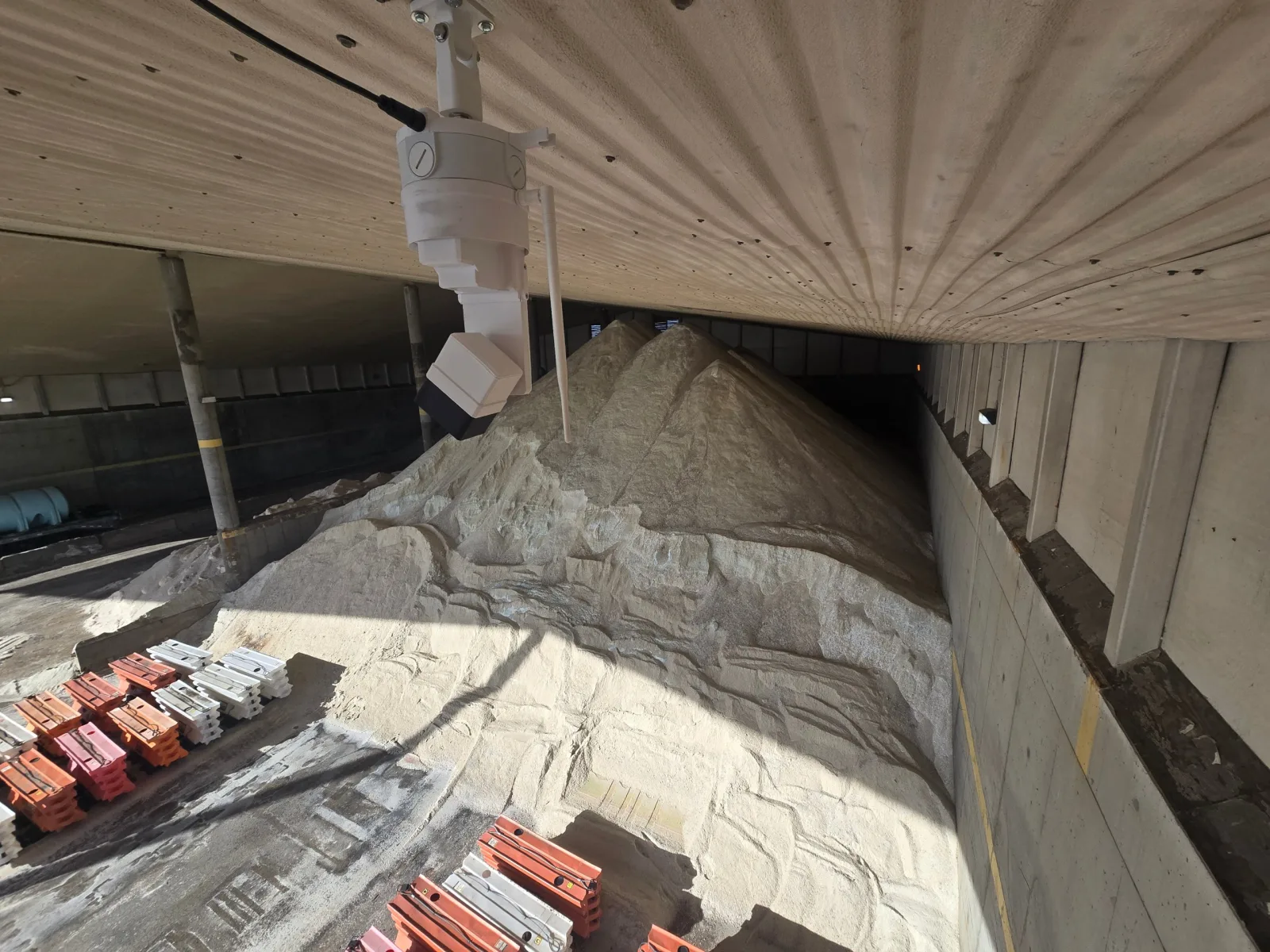 EOS2 LiDAR sensor under the roof of an open-front concrete salt shed, looking down on several conical road salt piles dumped along the back wall