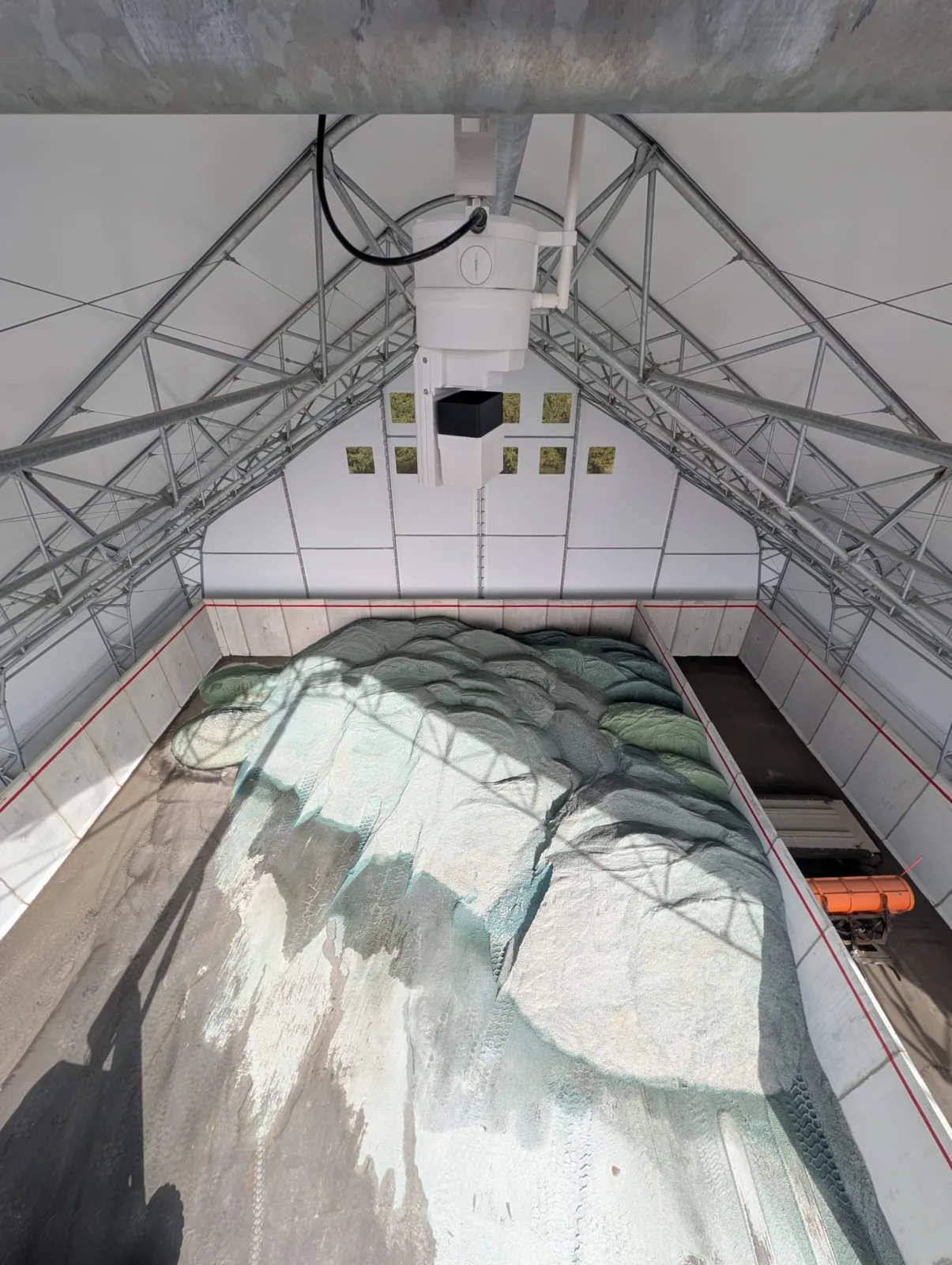 Treated road salt stockpile inside a pole-frame storage building with concrete walls, seen from the EOS2 sensor at the ridge, with a spreader truck parked beside the pile