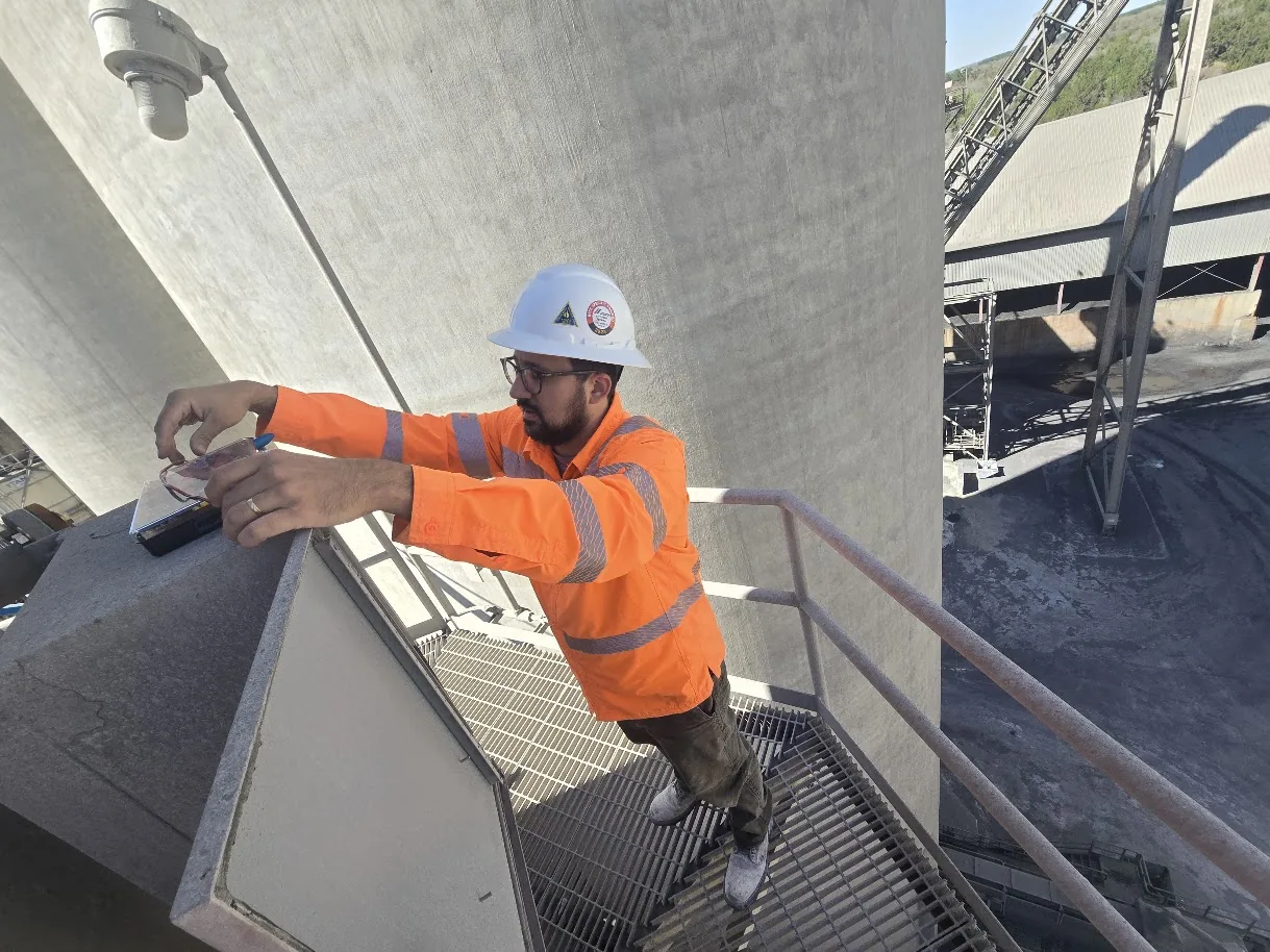 Altamus engineer in a hard hat and high-visibility shirt working on an elevated platform beside concrete silos at a cement plant